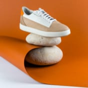 One shoe of beige and brown sneakers standing with his side view on top of two small rocks.