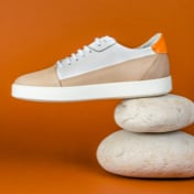 One shoe of beige and brown sneakers standing on top of two small rocks, only the heel touches the stones, with his side view shown.